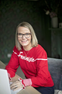 woman sat at table with laptop in a red jumper smiling at the camera